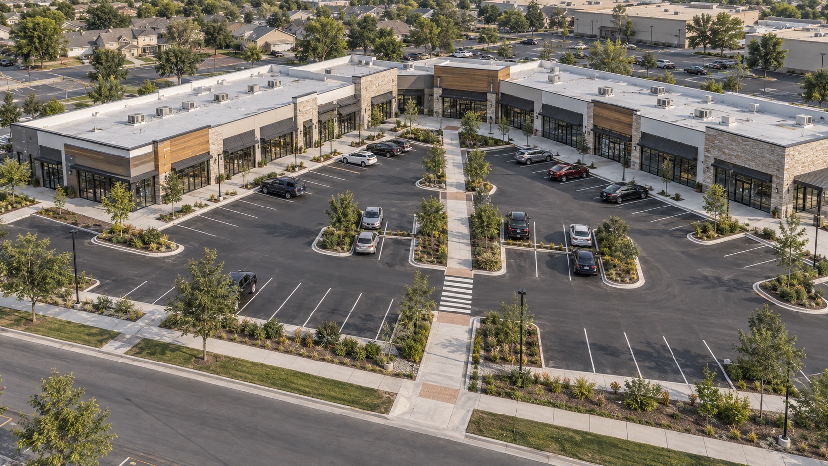 Higher aerial view of two retail wings around shared parking with a central pedestrian walkway leading to storefronts.